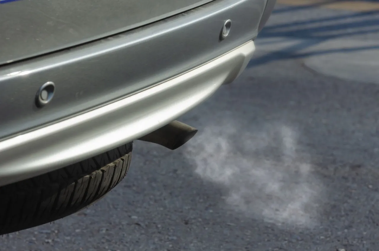 Rear bumper of a silver car with exhaust smoke drifting from the tailpipe across the asphalt